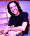 A smiling man with shoulder-length dark hair wearing a black t-shirt.