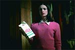 A woman in a pink sweater holds a carton of milk in a dimly lit room.