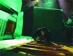 A person leans over a slatted wooden surface in a room illuminated by green light.