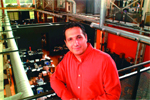 A man in a bright red button-down shirt smiles while standing on a balcony overlooking a multi-level office.