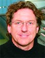 A man with curly brown hair and glasses smiling at the camera.