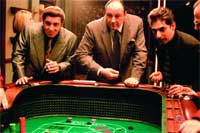Three men in formal suits leaning over a green felt gambling table in a dimly lit room.