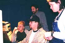 Four people look toward audio equipment in a dimly lit room.