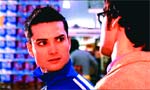 A man in a blue athletic jacket looks intently at a man wearing glasses and a tan coat.