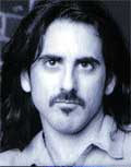 Close-up portrait of a man with long dark hair and a dark mustache looking forward.