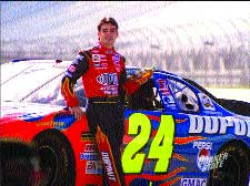 A man in a red and black racing suit stands next to a blue race car with the number 24.
