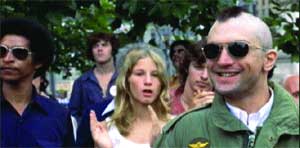 A group of people standing together outdoors, including a man with a mohawk and sunglasses.