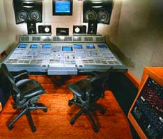 A large mixing console with two black office chairs in a recording studio.