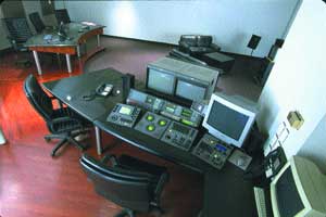 An office with several desks, black chairs, and multiple computer monitors on a dark floor.