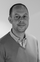 Black and white headshot of a man with short hair wearing a collared shirt and a V-neck sweater.