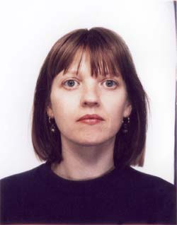A woman with shoulder-length brown hair and bangs looks directly at the camera against a white background.