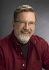 A man with a beard and glasses wearing a red shirt smiles.