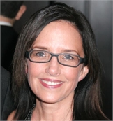 A smiling woman with dark hair and rectangular glasses looking toward the camera.