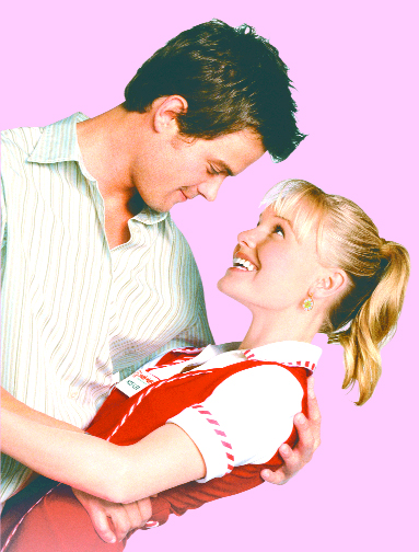 A man in a striped shirt and a woman in a red and white uniform embrace and smile at each other.