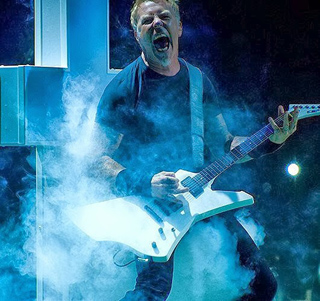 A man with an open mouth plays a white electric guitar surrounded by blue-tinted smoke.