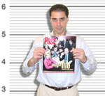 A man in a white shirt holds up a magazine against a black and white height measurement background.