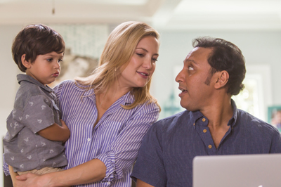 A woman holds a young child while looking toward a man sitting next to her.