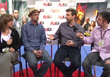 Four people sit in a row on stools, engaged in a conversation in front of a branded backdrop.
