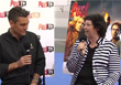 A man in a black shirt and a woman in a striped jacket talk into microphones during an interview.
