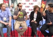 Four people sit in a row on a stage during a panel discussion with a branded backdrop.