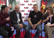 Four people sit in a row on chairs during a panel discussion in front of a branded backdrop.