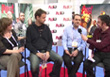 Four people sit in a row for a panel discussion at an indoor event.