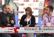 A man in a black shirt, a woman in a black blazer, and a man in a pink striped shirt sit at a panel.