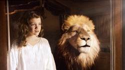 A young girl in a white shirt looks toward a large, realistic lion head sculpture.