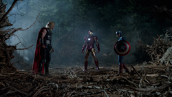 Three superheroes stand in a dark, smoky forest clearing among debris.
