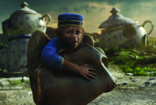 A small monkey in a blue shirt and hat hugs a large brown object amidst broken porcelain.