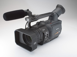A professional black video camera equipped with a large shotgun microphone and a viewfinder.