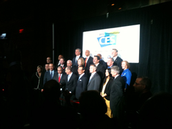 A large group of men and women in suits and dresses stand together on a stage in front of a screen with the CES logo.