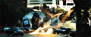 Multiple cars colliding and flipping in a city street amidst sparks and smoke.