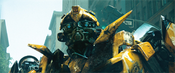 A large, weathered yellow robot stands in a city street looking toward the camera.