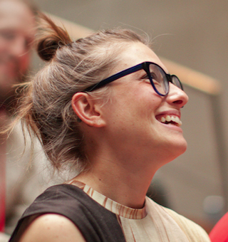 A smiling woman with brown hair in a bun and dark-rimmed glasses looking upward.