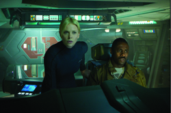 A blonde woman and a Black man look intensely ahead while seated in a dimly lit, high-tech spaceship cockpit.