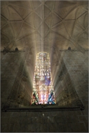 Sunlight beams through a tall, colorful stained-glass window in a vaulted stone cathedral.