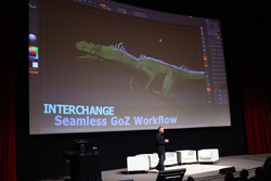 A man stands on a stage in front of a large projection of a 3D dinosaur model and text.