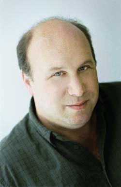 A middle-aged man with thinning hair and blue eyes smiling slightly against a light background.