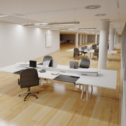 An open-plan office with white desks, black chairs, and light wood flooring under bright ceiling lights.