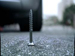 A silver metal screw standing vertically in the middle of a dark asphalt road.