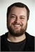 A smiling man with short brown hair and a full beard wearing a black shirt.