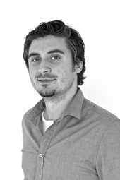 Black and white portrait of a man with dark hair and a light beard wearing a button-down shirt.
