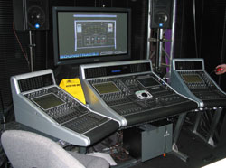 Three digital audio mixing consoles arranged in a row in front of a computer monitor.