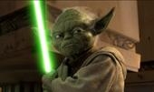 A small green creature with large ears holds a glowing green lightsaber.