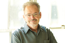 A middle-aged man with graying hair and glasses smiling while wearing a gray button-down shirt.