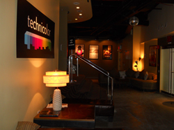 A Technicolor sign on a wall next to a lamp and a staircase leading to a lounge with sofas.
