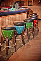 A line of four bar stools with green, blue, and red seats in front of a bar counter.