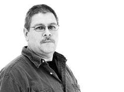 Black and white portrait of a man wearing glasses and a button-down shirt against a white background.