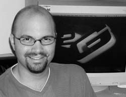 A smiling man with glasses and a goatee sitting in front of a computer monitor.